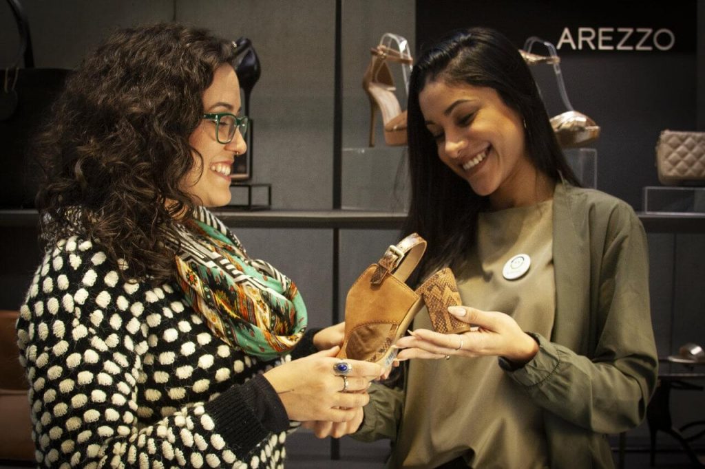 Duas mulheres conversando sobre um produto da Arezzo&Co.